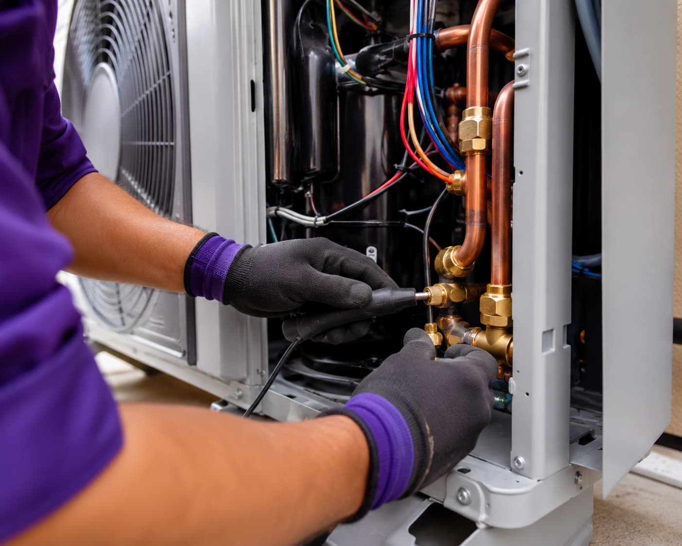 Close-up of a technician in a purple uniform repairing a heat pump unit in Sherman Oaks, CA.