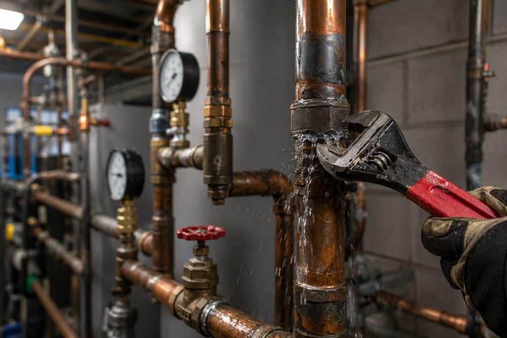Gloved plumber using a pipe wrench to repair a leaking copper fitting in a commercial mechanical room